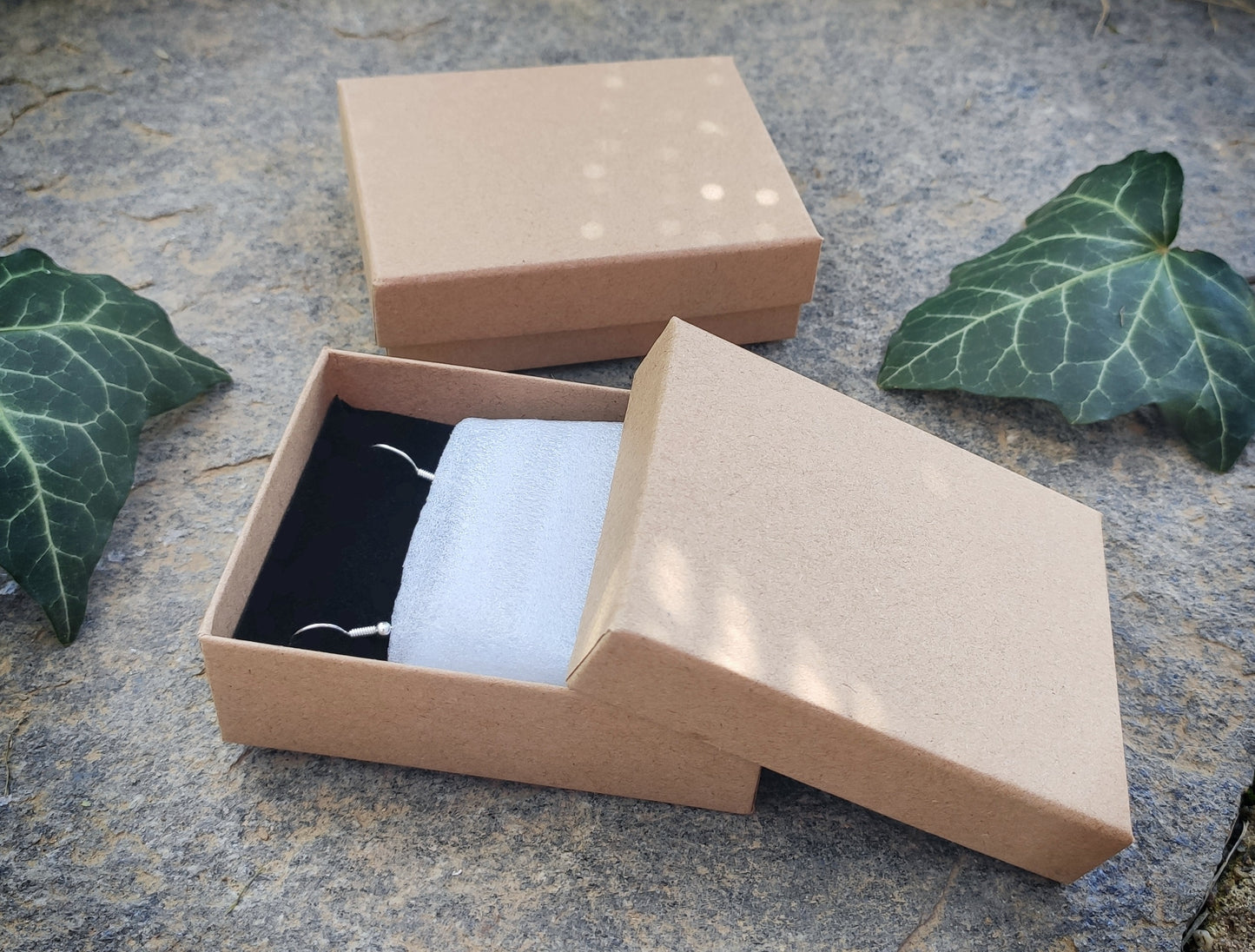 Gift box on a stone surface with leaves. The image shows that the earrings arrive gift ready and securely.