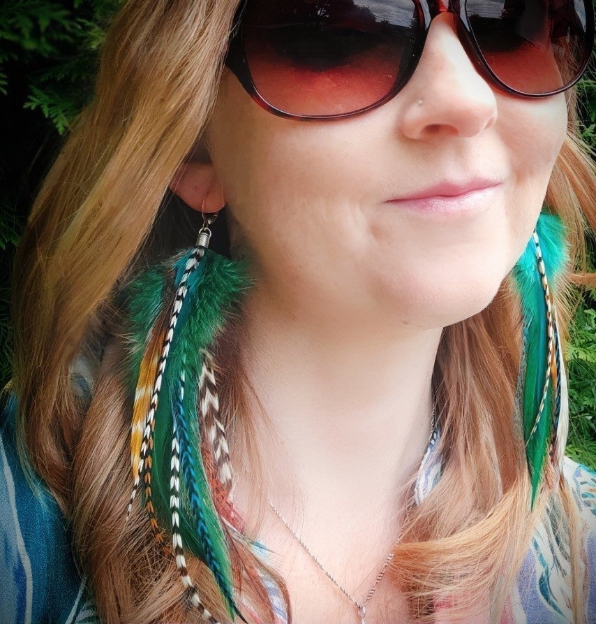 A model wearing green, white, blue and brown stripy feather earrings in a natural boho hippie style.