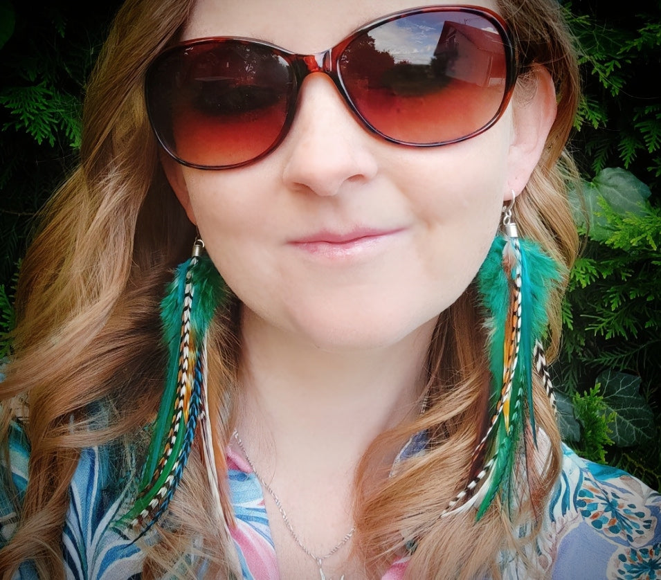 A model wearing colorful green, white and brown stripy feather earrings in a rustic bohemian style. She is outside in the summer.