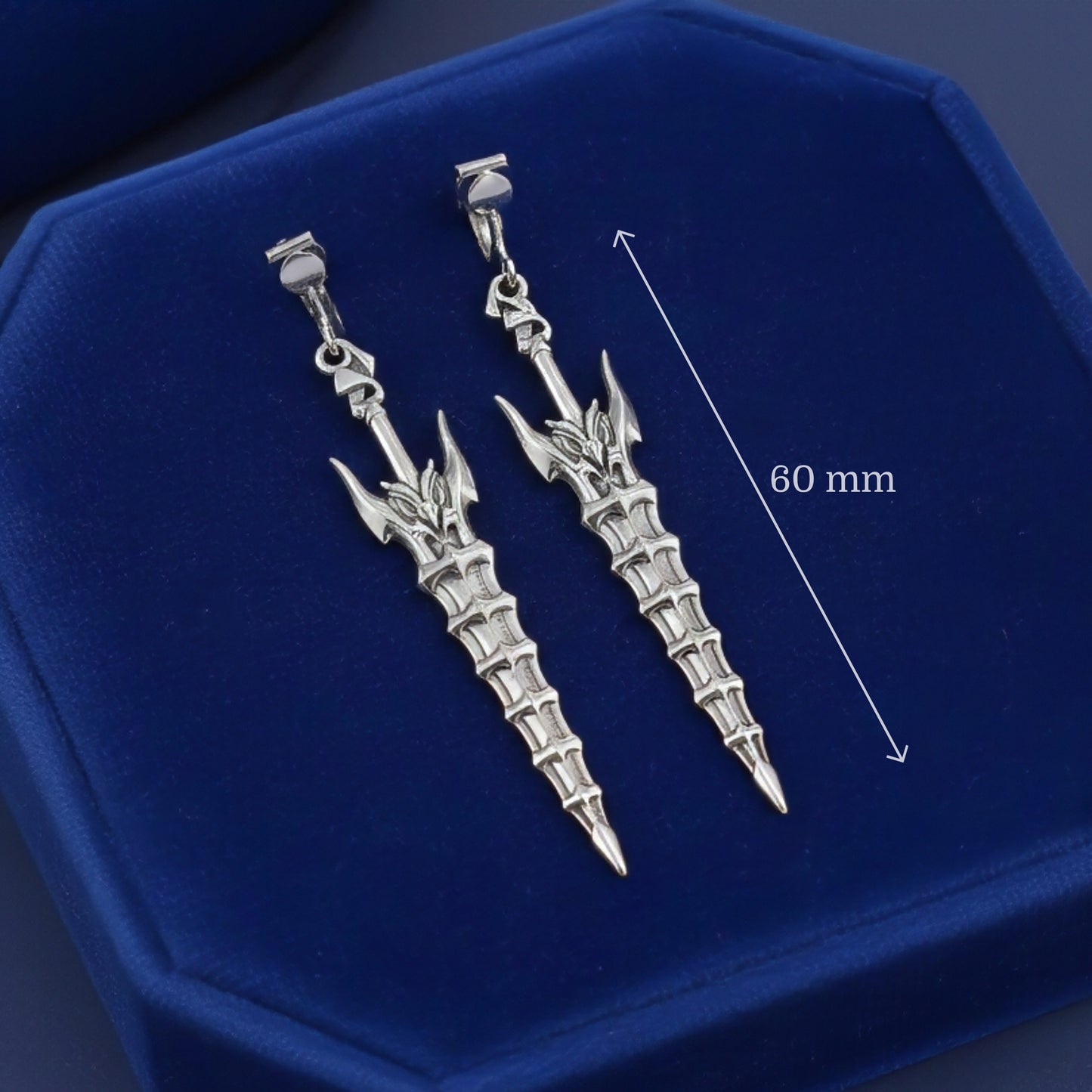 Fantasy silver sword earrings with clip-ons on a blue background with measurements shown