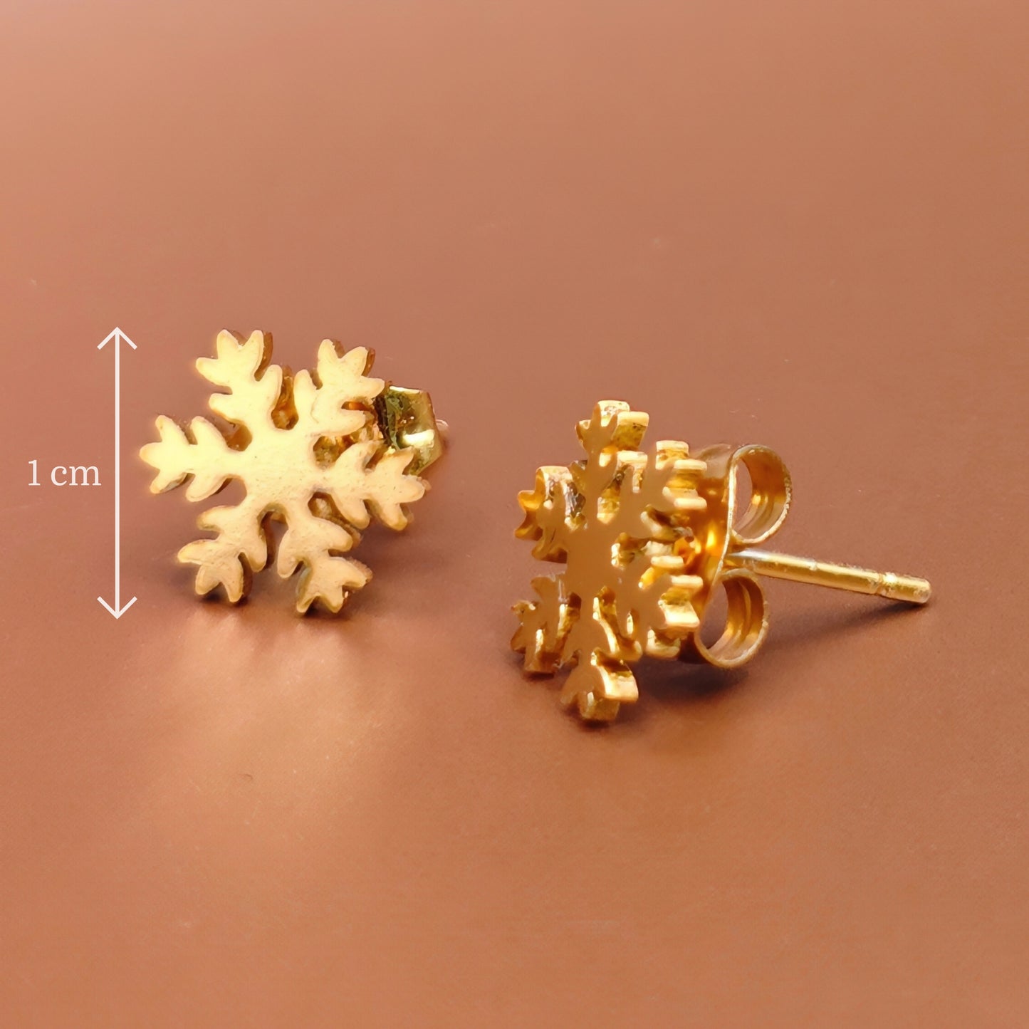 Gold snowflake stud earrings on a brown background with a measurement label.