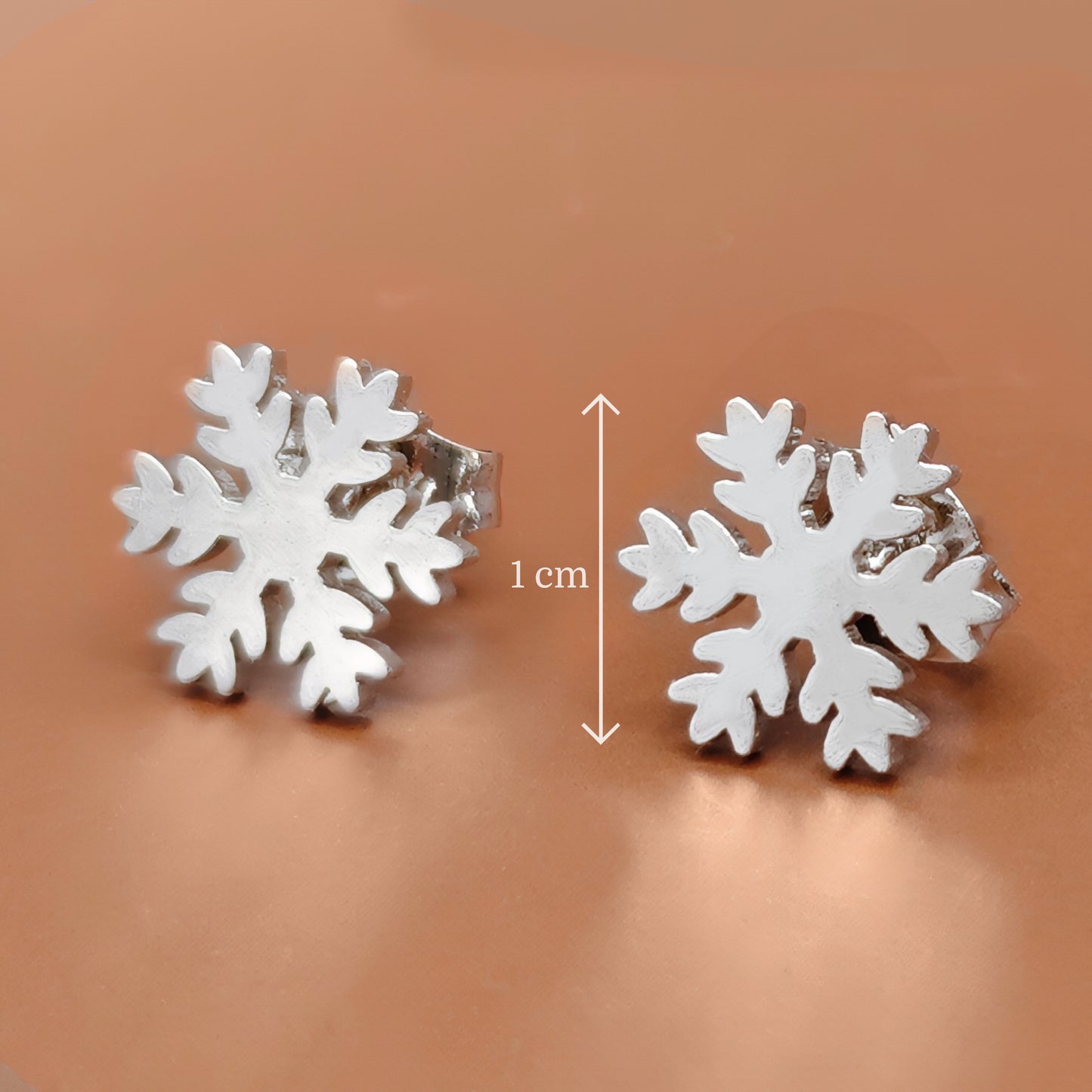Silver snowflake earrings on a brown background with a measurement label.