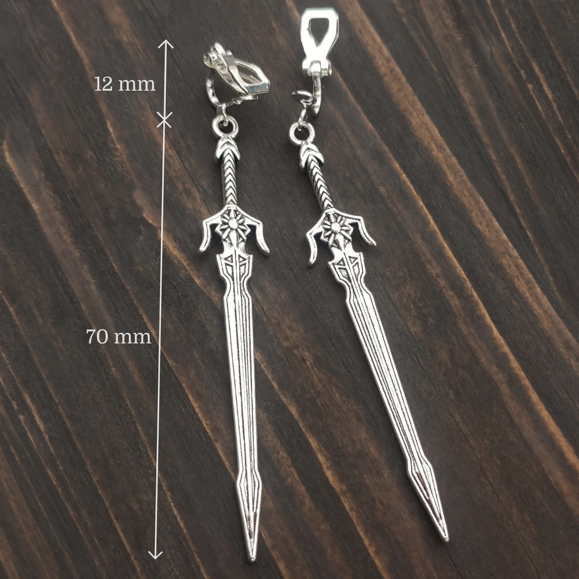 Silver sword clip on earrings on a wooden surface with measurements indicated.
