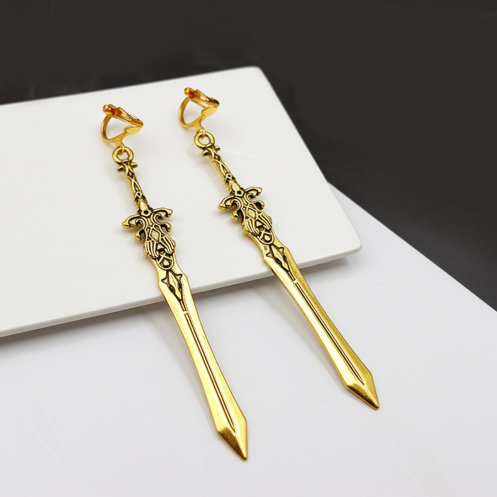 Gold sword earrings with clip ons on a white surface with a dark background. Fantasy medieval jewelry