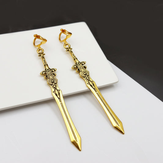 Gold sword earrings with clip ons on a white surface with a dark background. Fantasy medieval jewelry