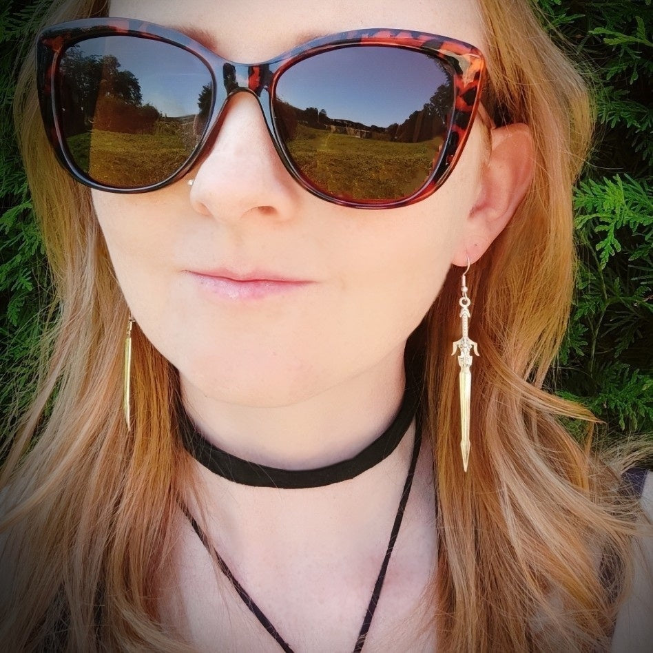 A female model wearing long silver sword earrings, in a fantasy medieval style. 