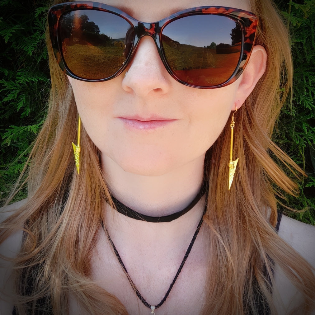 Woman wearing gold fantasy axe earrings with a blurred natural background