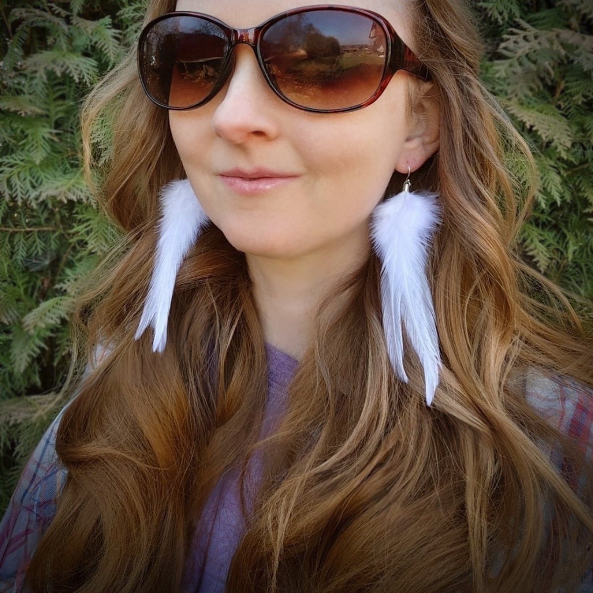 Woman wearing white feather earrings with a green natural background. Rustic bohemian style