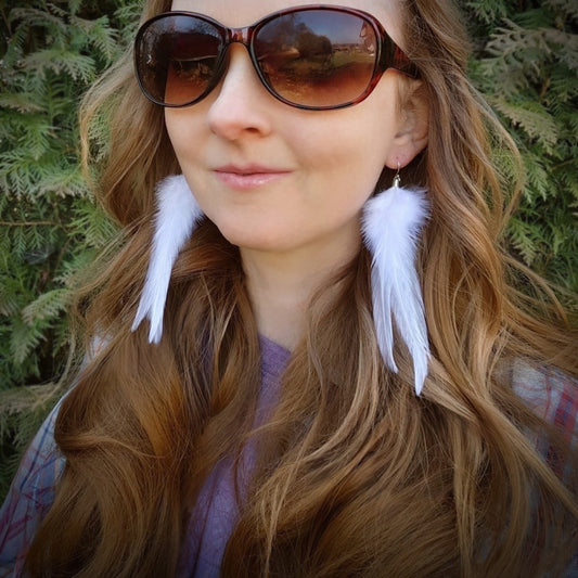 Woman wearing white feather earrings with a green natural background. Rustic bohemian style