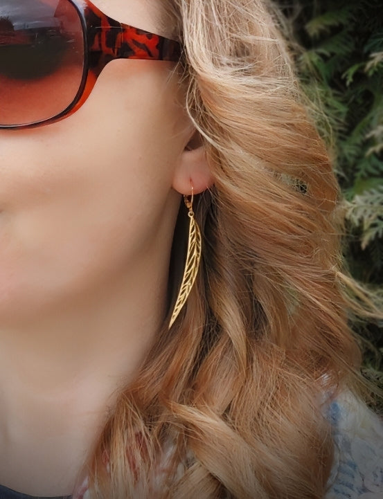 Woman wearing long pointy gold stainless steel leaf earrings with hoops