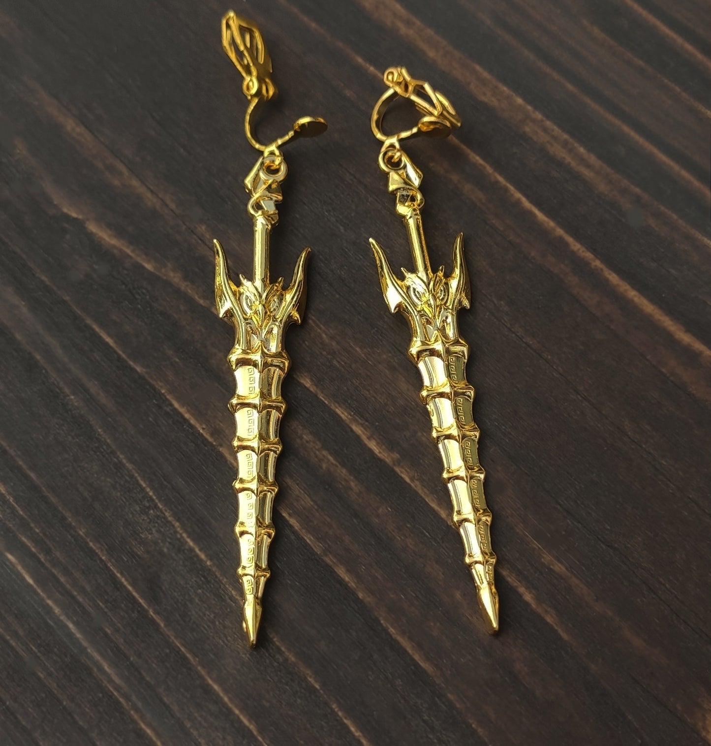 Fantasy style gold sword earrings with clip-ons, on a wooden background