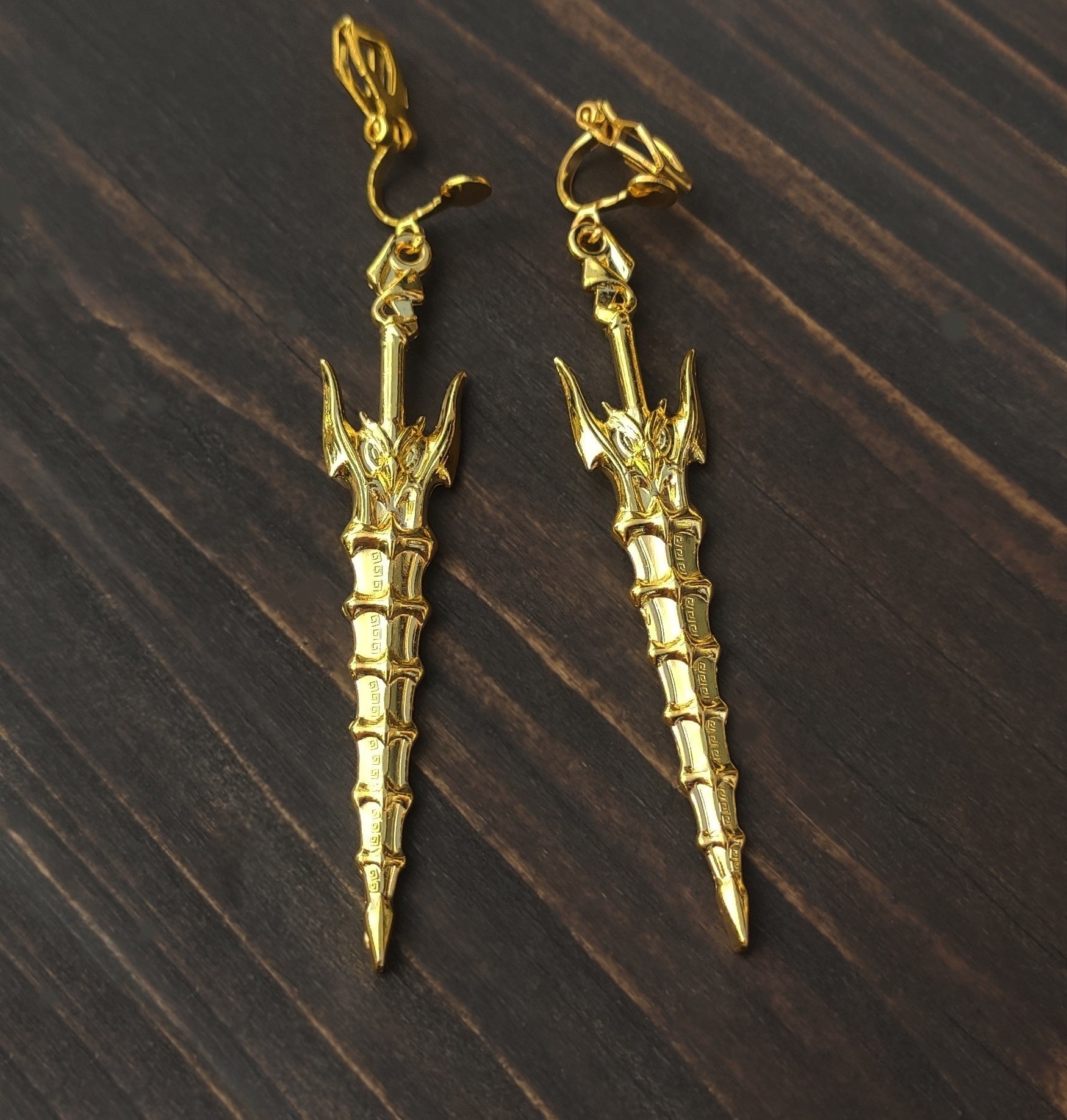 Fantasy style gold sword earrings with clip-ons, on a wooden background