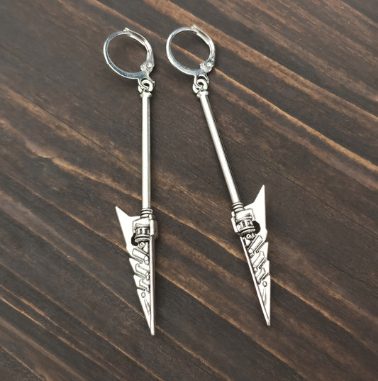 Silver arrow-shaped sword earrings with hoops on a wooden surface. Fantasy battle mace