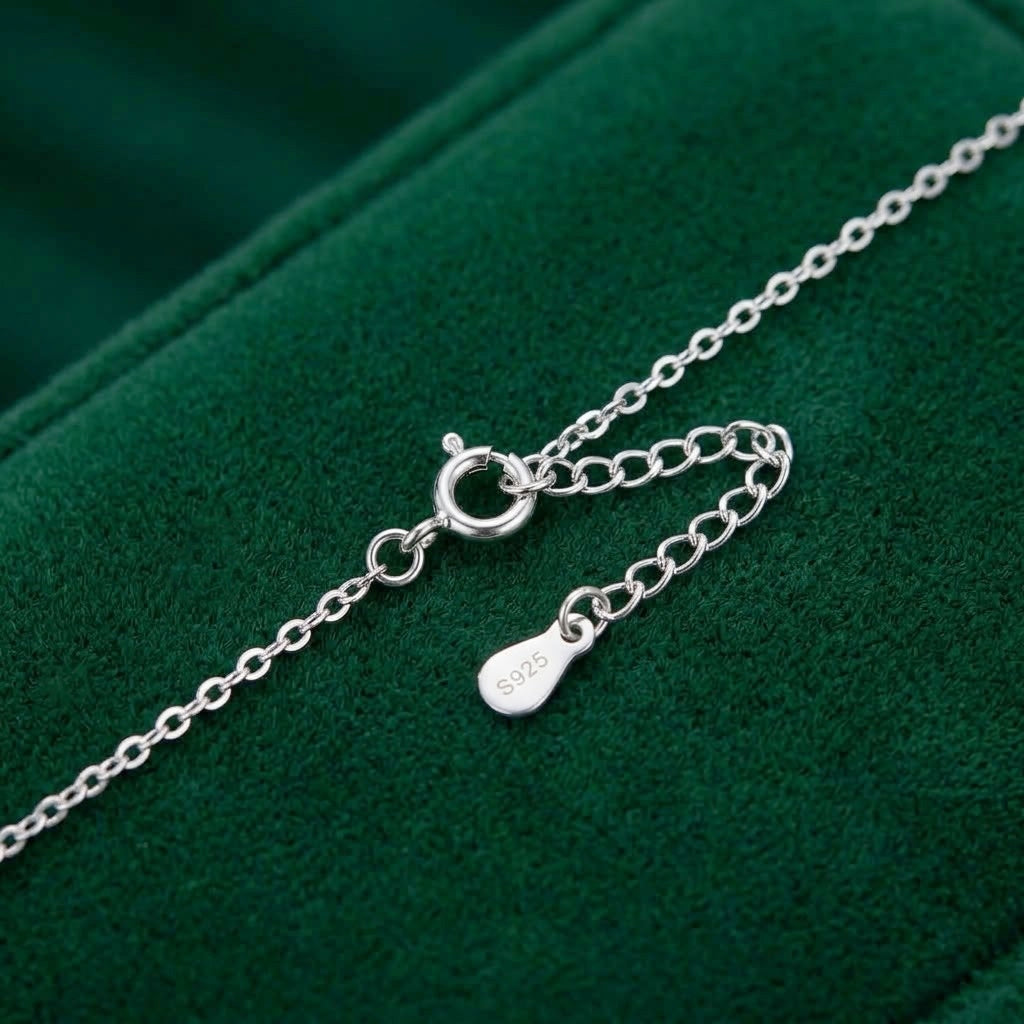 A close-up of a silver chain necklace with a lobster clasp and an adjustable extender chain featuring a small S925 engraved tag, displayed on a dark green velvet surface.