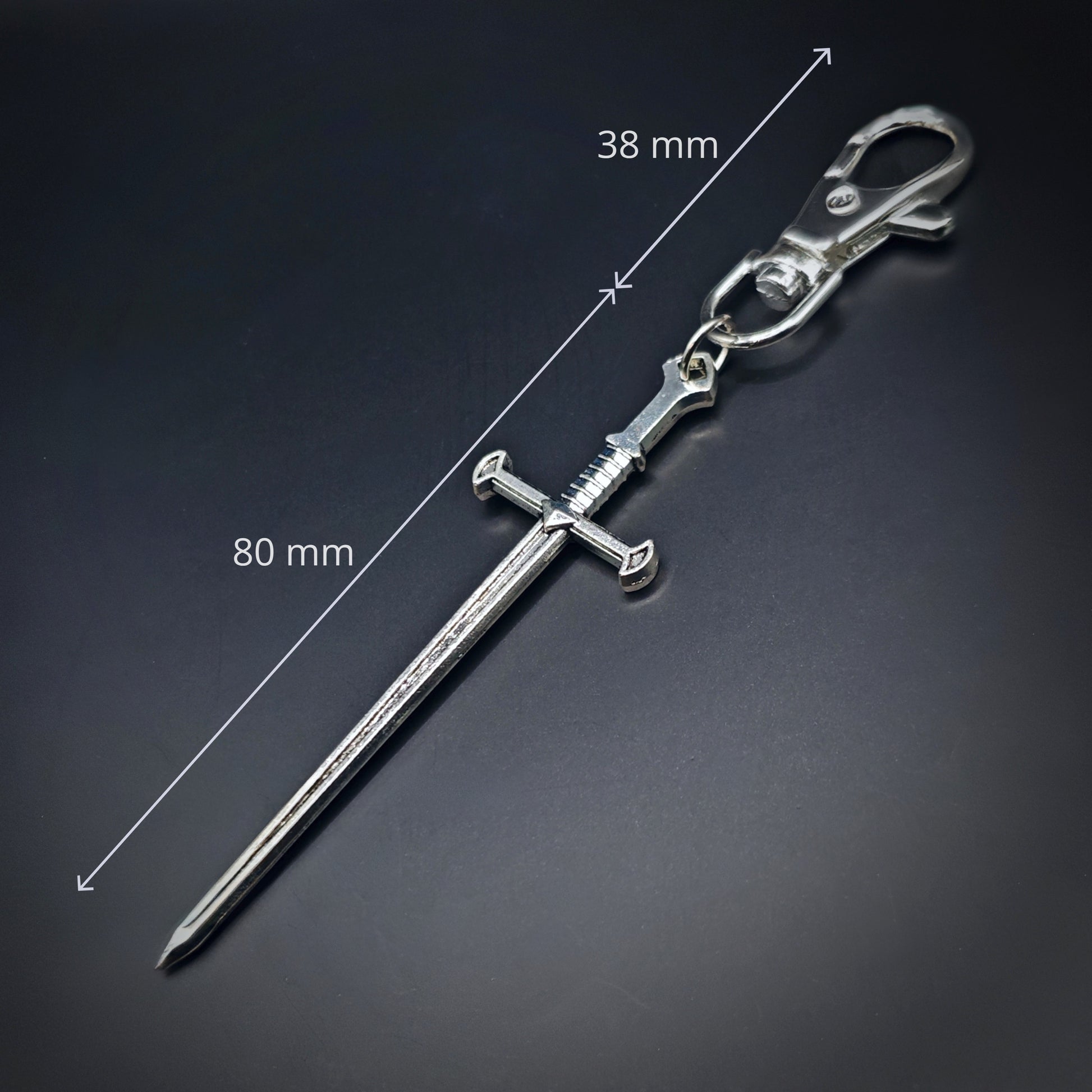 Silver sword-shaped keychain with measurements on a dark background