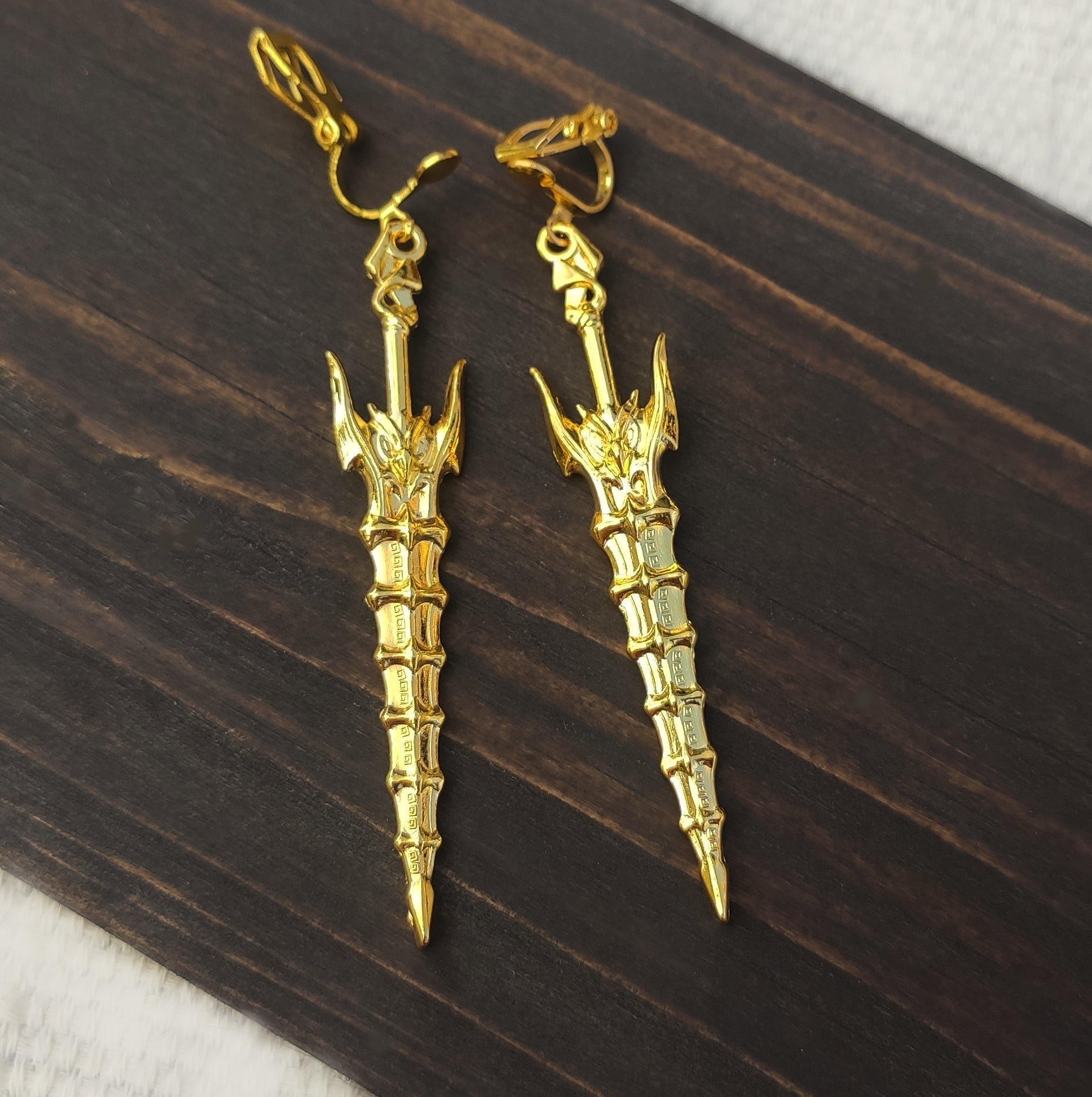 Gold clip on sword earrings on a wooden background
