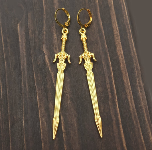 Long gold sword earrings with leverback hoops on a wooden background. Medieval fantasy style