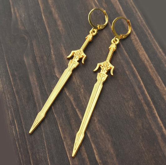 Long gold sword earrings with leverback hoops on a wood background. 