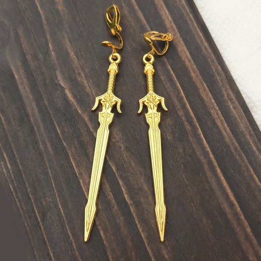 Long gold swords dangle from clip on earrings on a wooden background
