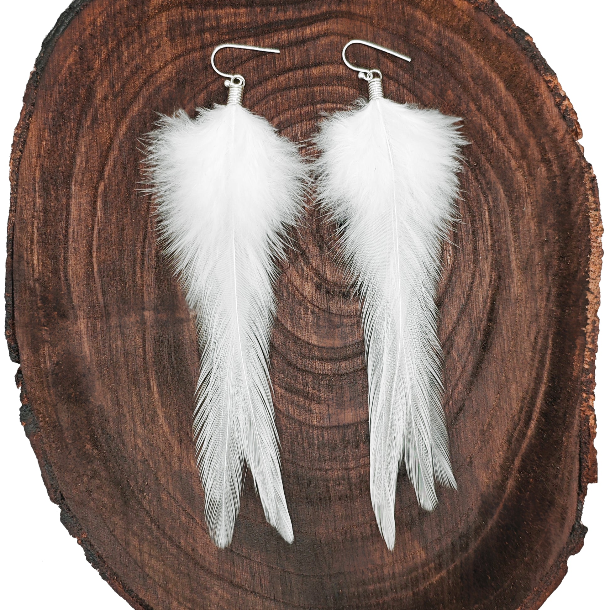 White feather earrings on a wooden surface. Boho hippie jewelry