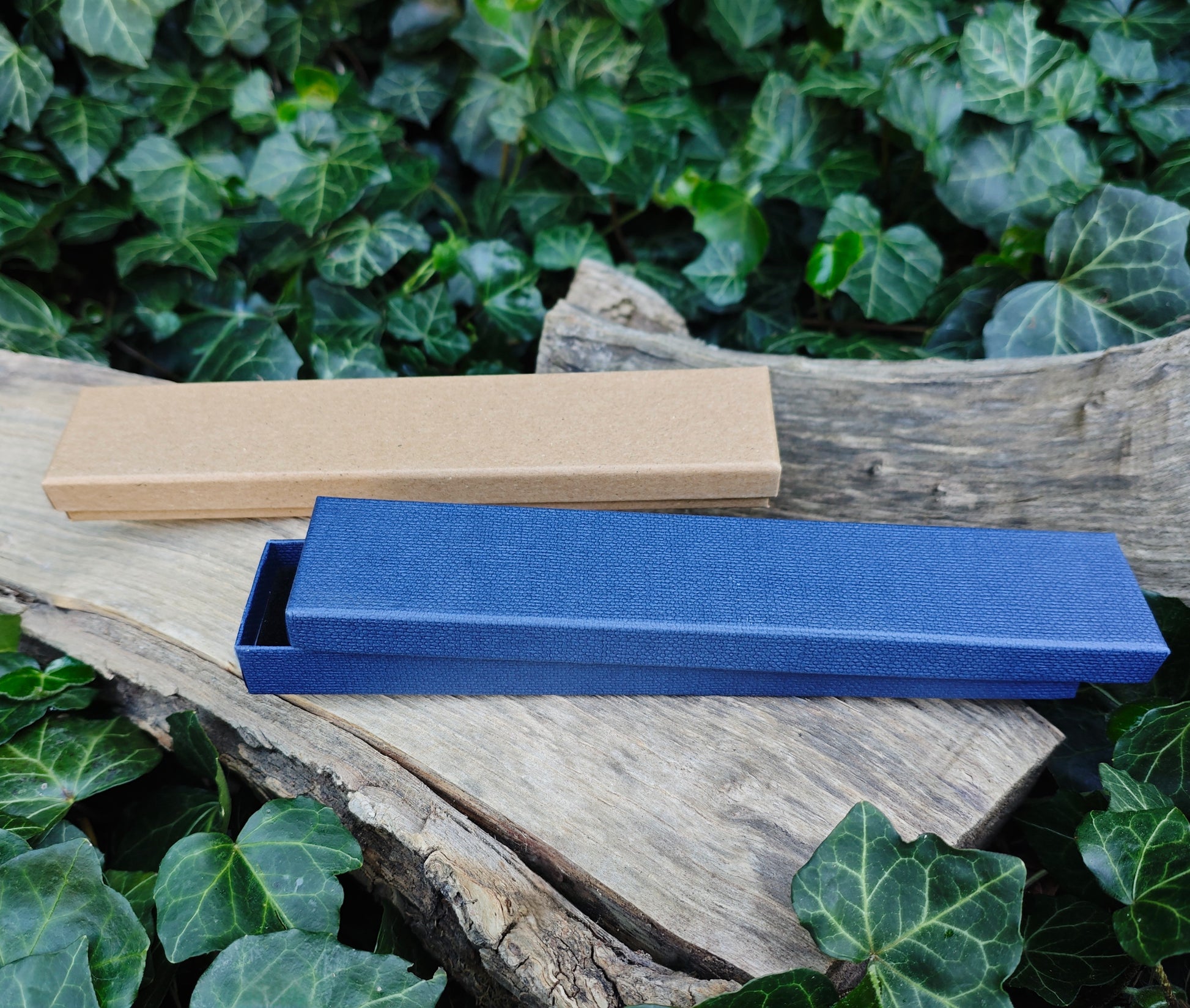 Blue and beige gift boxes on a wooden surface with green foliage in the background