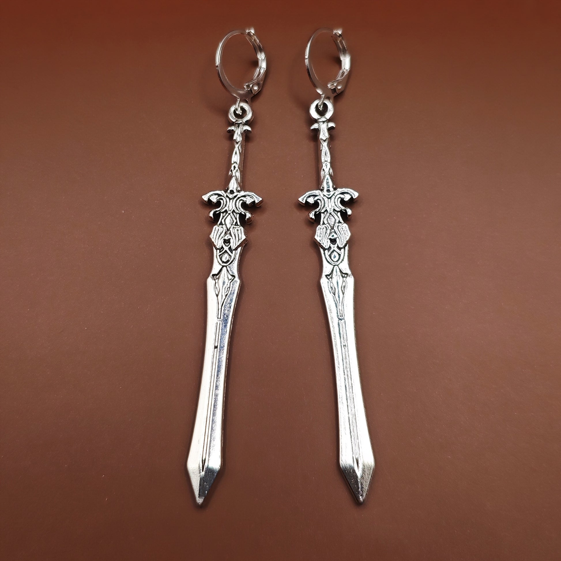 Medieval-style silver sword earrings with stainless steel huggie lever back hoops, perfect for fantasy fashion and cosplay.