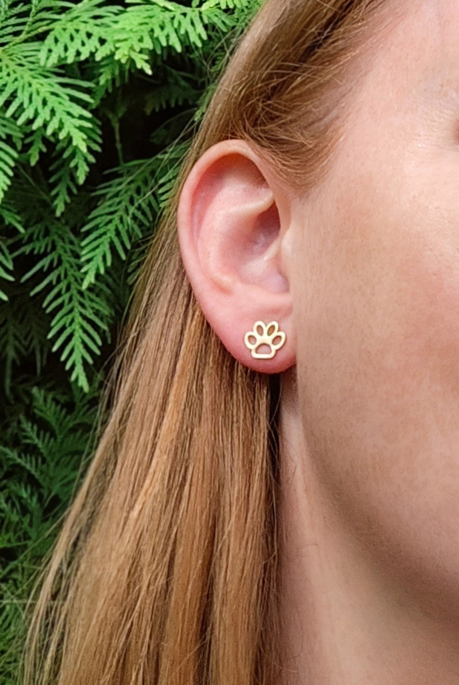 Gold paw print earring worn by a person with green foliage in the background
