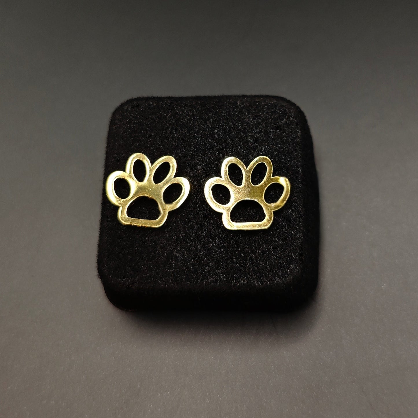 Gold paw print earrings on a black stand against a dark background