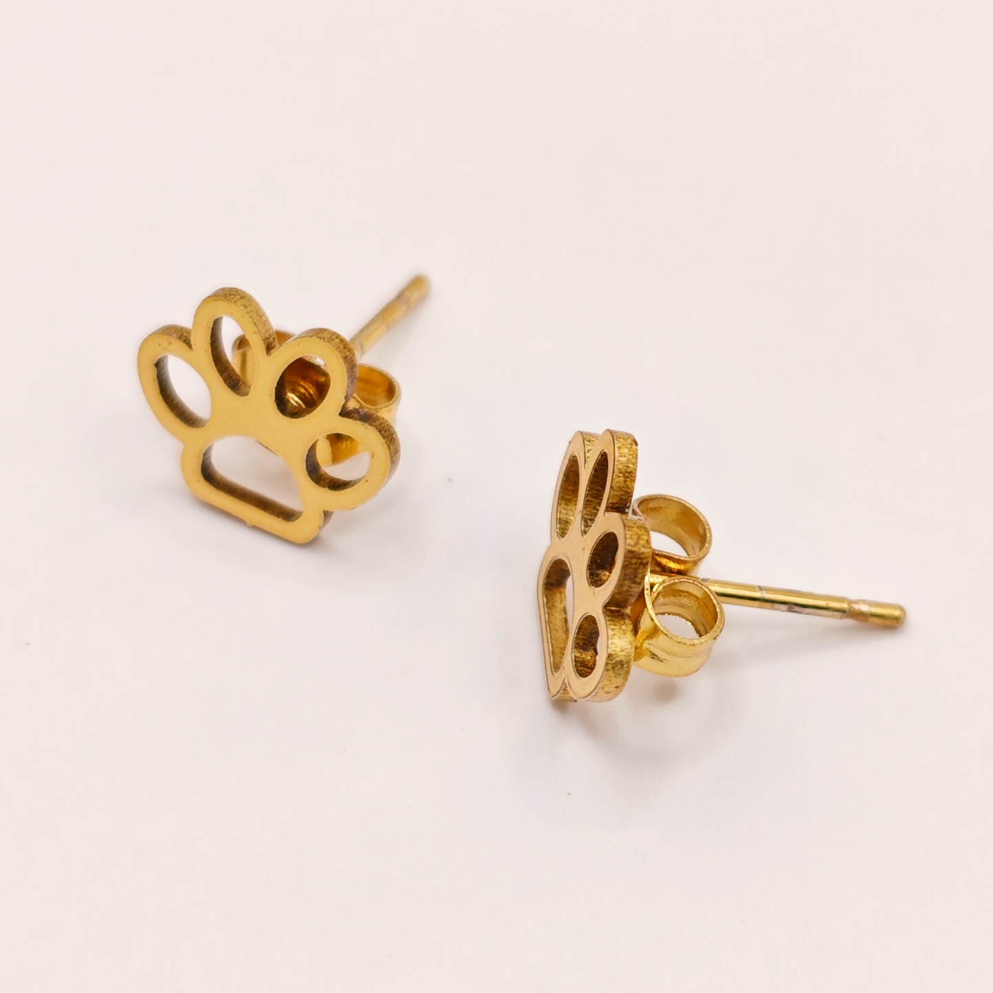 Gold dog paw print earrings made with stainless steel on a light beige background.