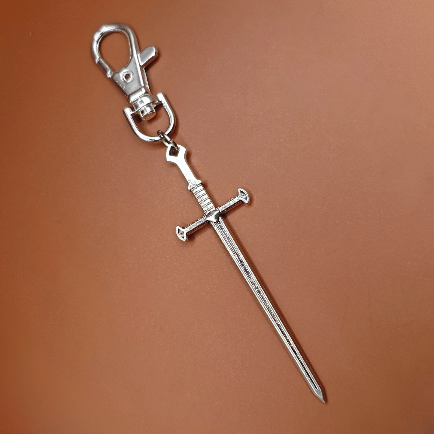 Silver sword keychain with lobster clasp on a brown background. Fantasy medieval style.