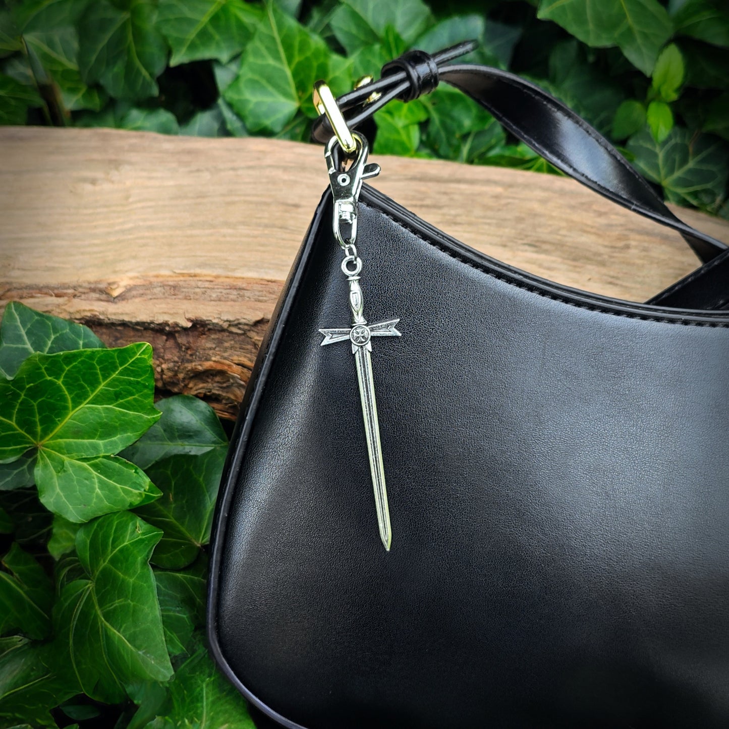 Black handbag with a silver sword bag charm against a natural background