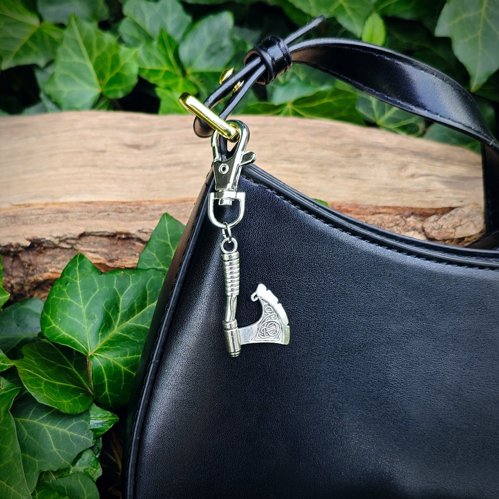 Black handbag with an axe bag charm against a natural background