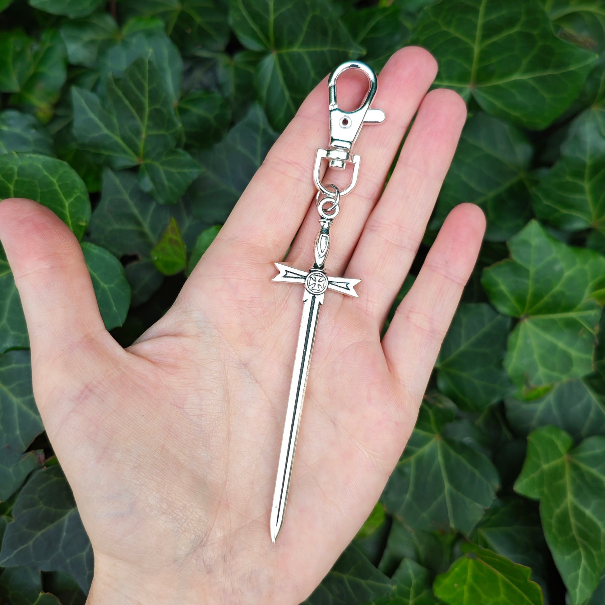 Silver sword keychain held in a hand with a green leafy background