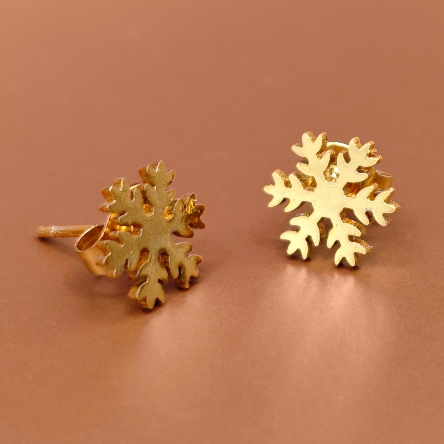 Gold snowflake earrings on a brown background. Winter jewelry for her.