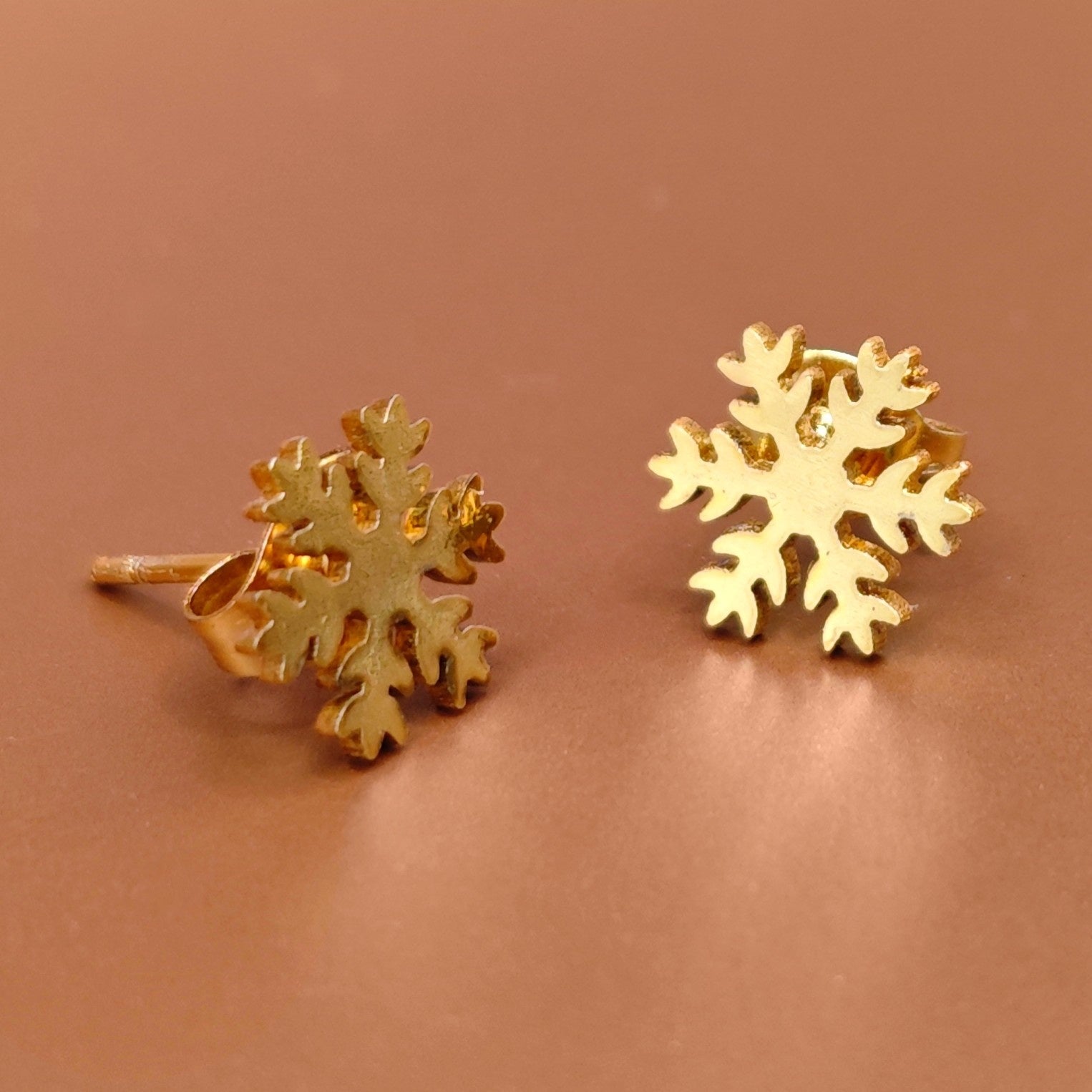 Gold snowflake earrings on a brown background. Winter jewelry for her.
