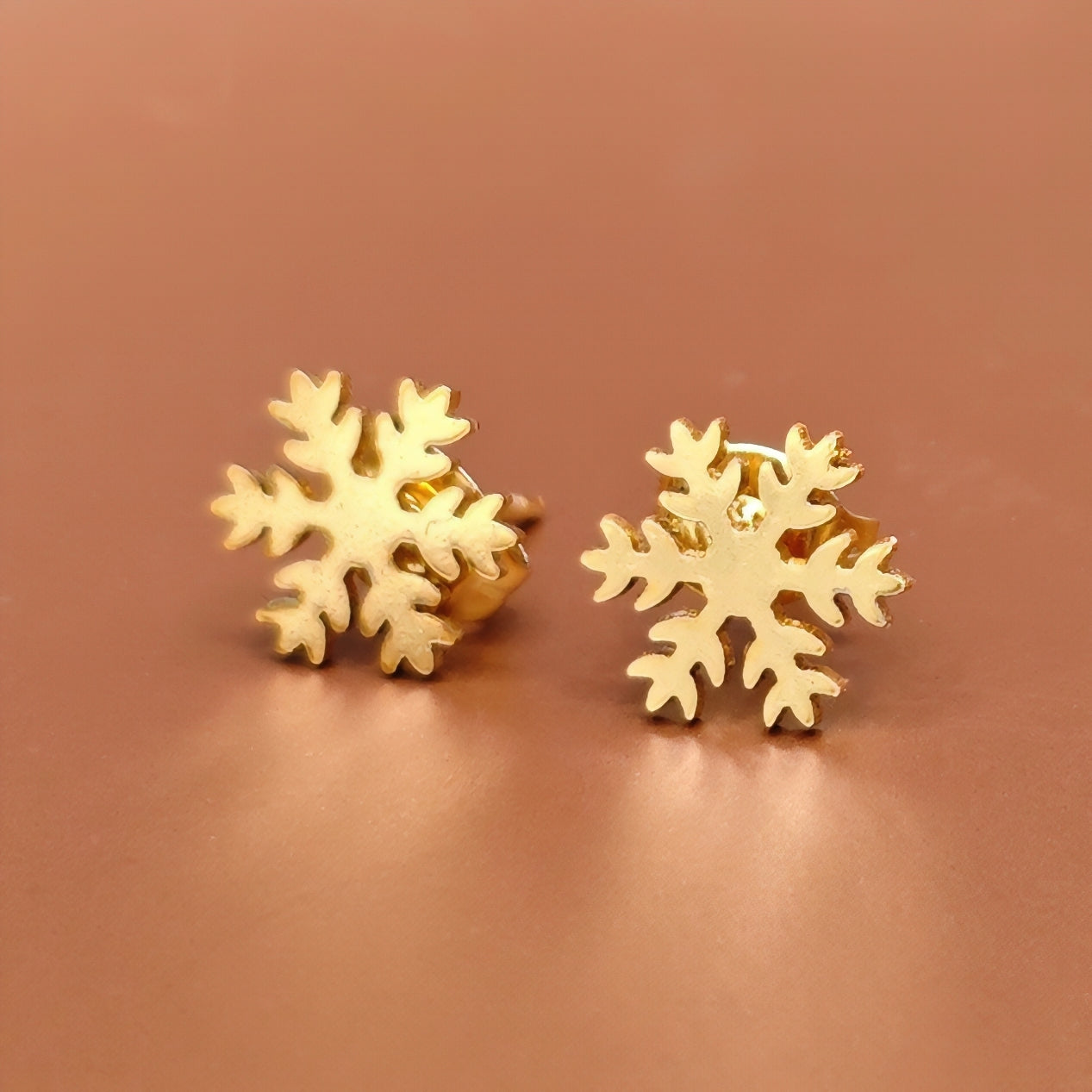 Gold snowflake earrings on a brown background. Festive Christmas jewelry