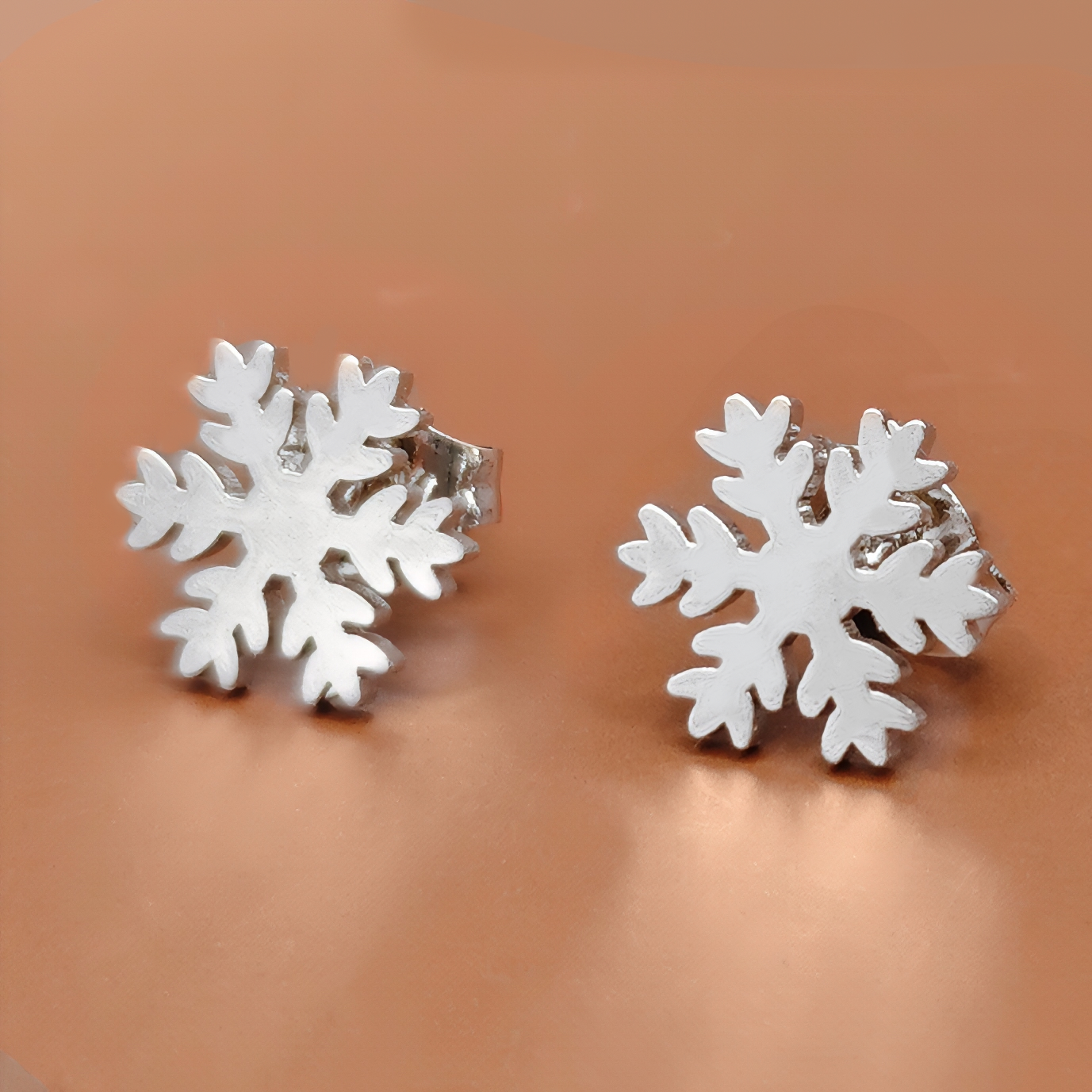 Silver snowflake stud earrings on a brown background. Winter jewelry