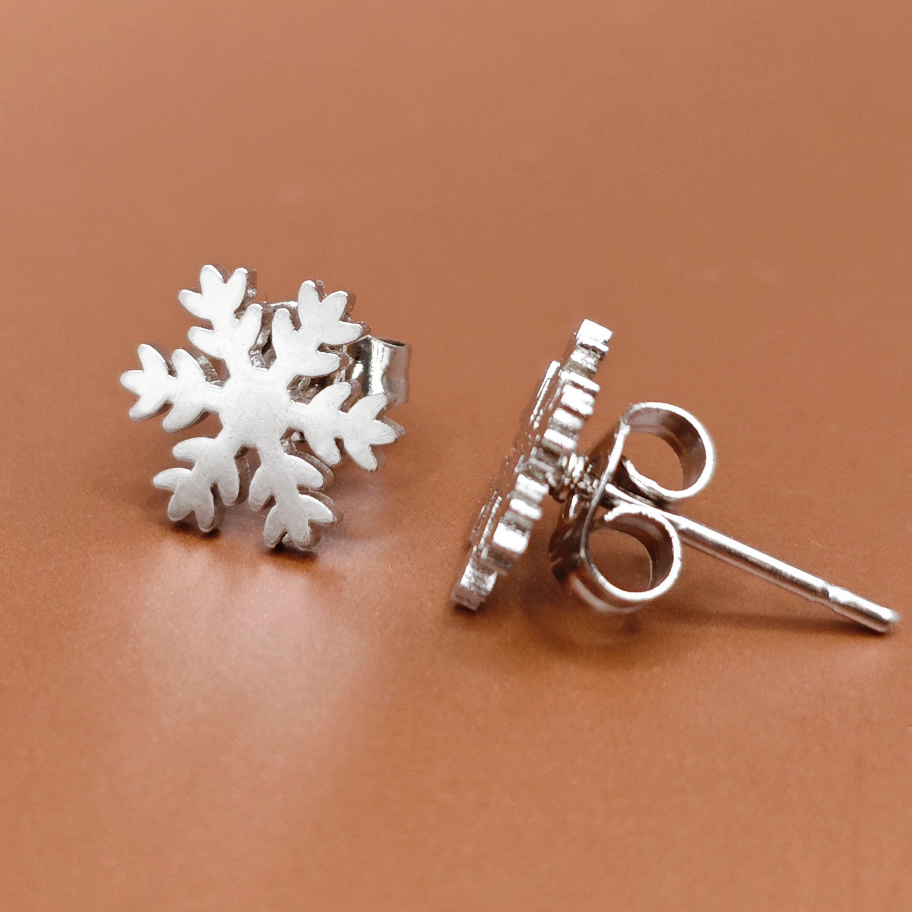 Silver snowflake earrings on a brown background. Xmas jewelry for the holiday season