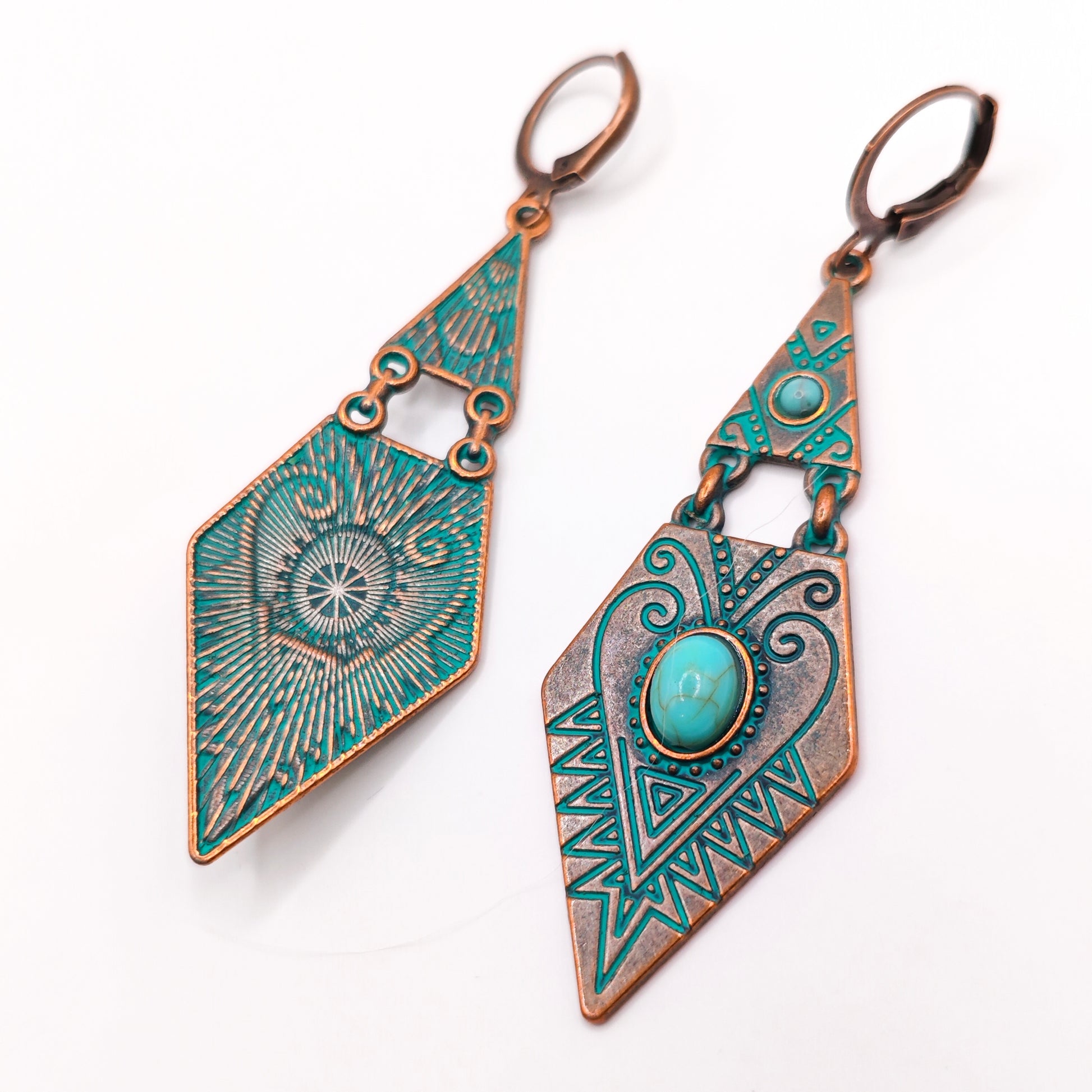 Pair of earrings with geometric design and turquoise stone on a white background. One of the earrings is turned over to show the metal back