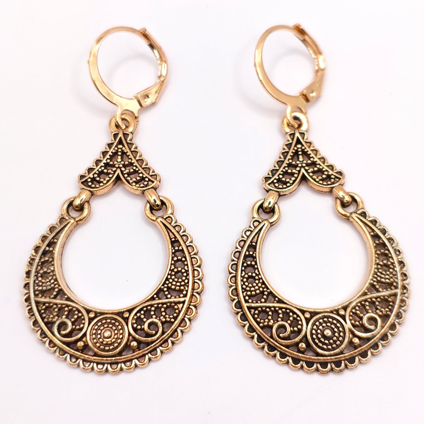 Pair of bohemian gold dangle hoop earrings with intricate filigree designs on a white background