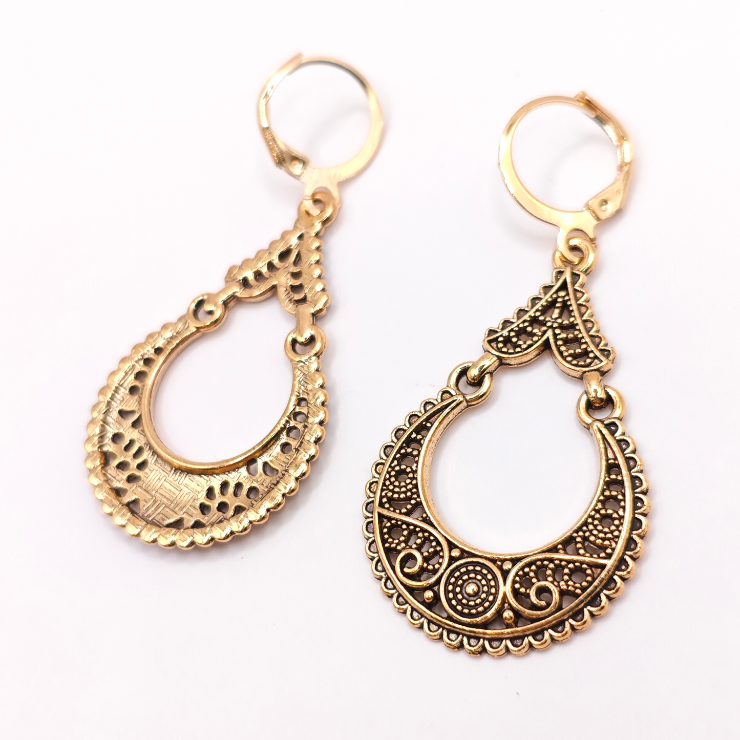Pair of gold hoop earrings with intricate designs on a white background. One earring is turned over showing the metal back