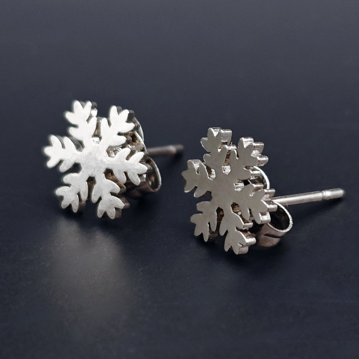 Silver snowflake stud earrings on a dark background, festive Christmas jewelry