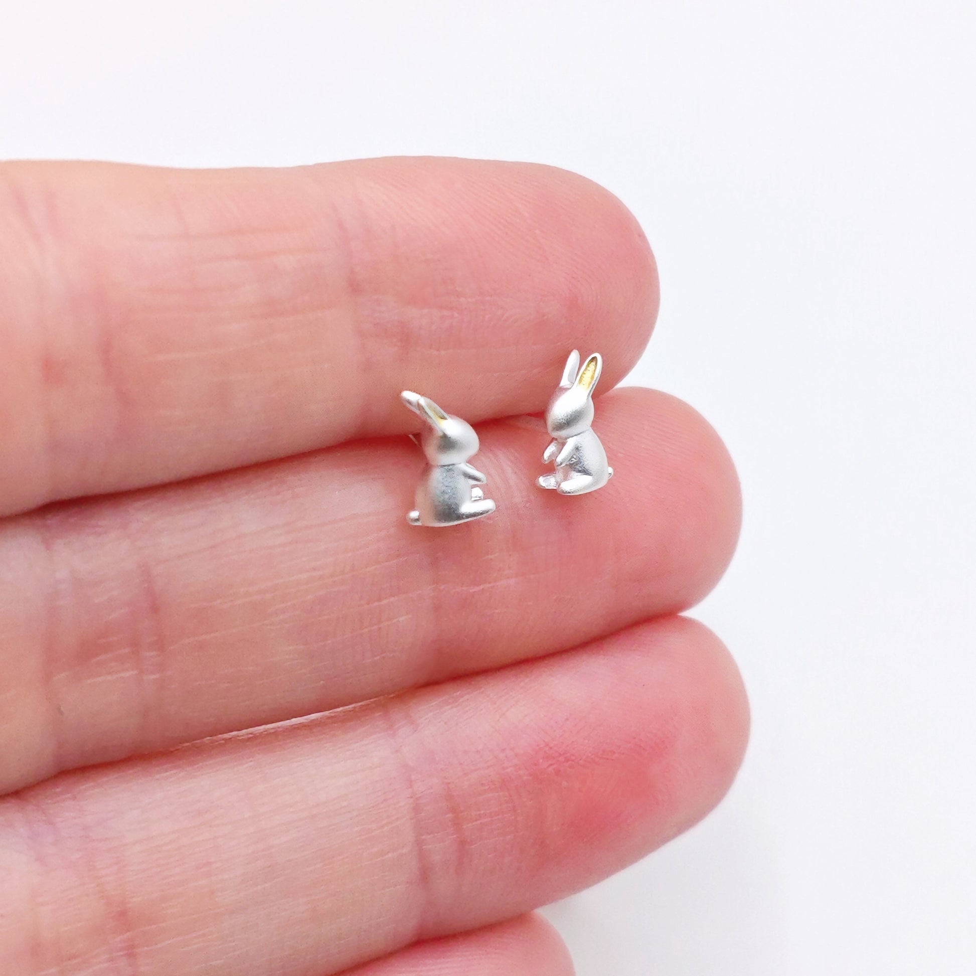Silver rabbit-shaped earrings on a hand with a white background