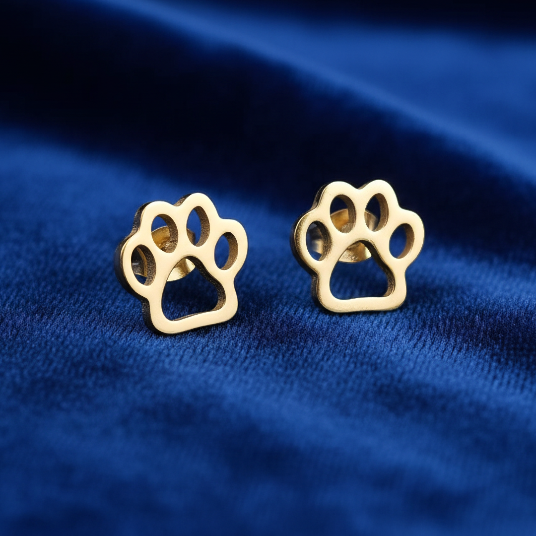 Gold paw print earrings on a blue fabric background