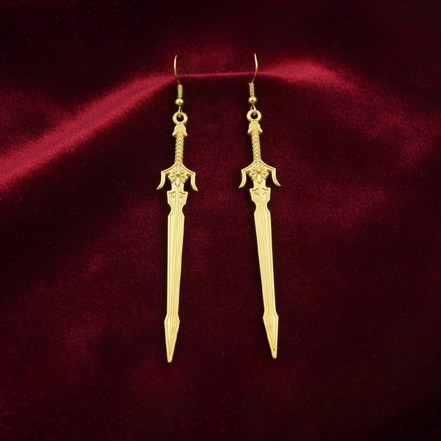 Medieval style fantasy long gold sword earrings with hooks on a red background