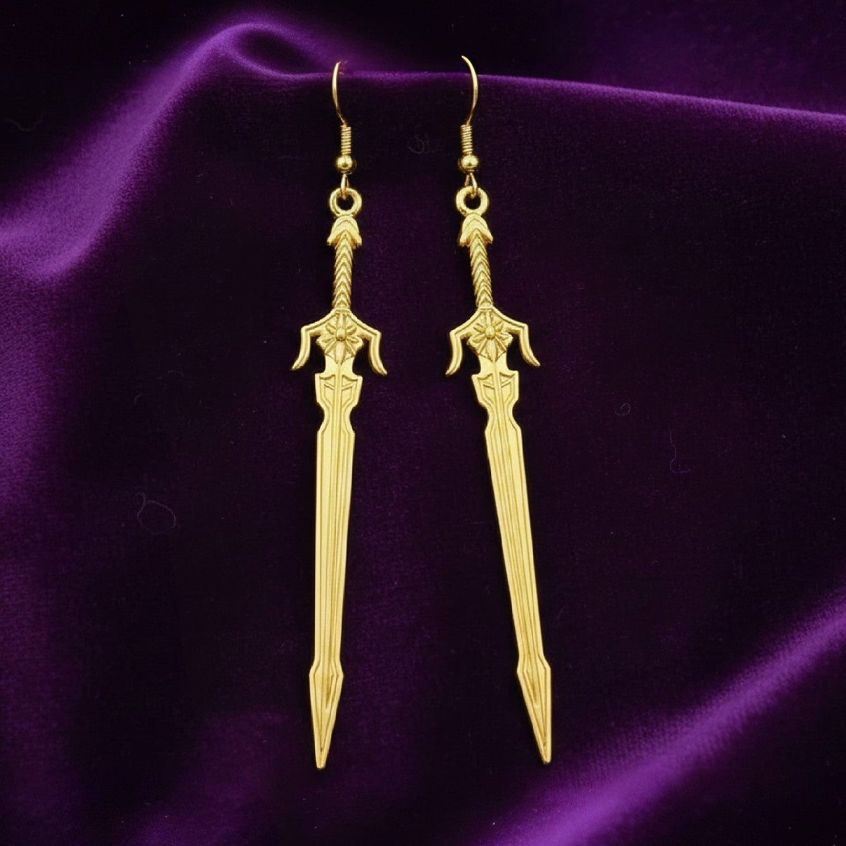 Medieval style fantasy long gold sword earrings with hooks on a purple background