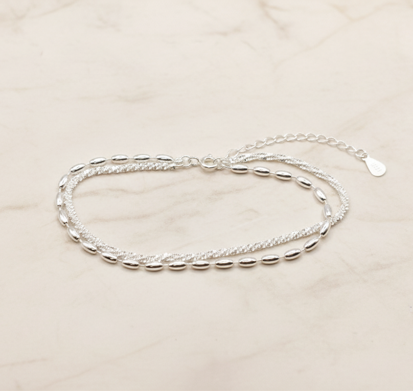 925 Silver Bracelet featuring a double chain, one twisted sparkle chain and one with oval beads, on a marble background