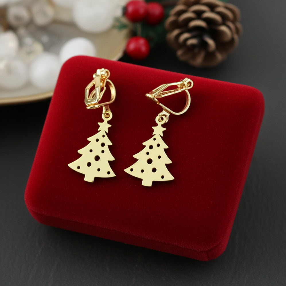 Festive Christmas tree earrings with clip-ons made from gold stainless steel on red velvet with lights in the background.
