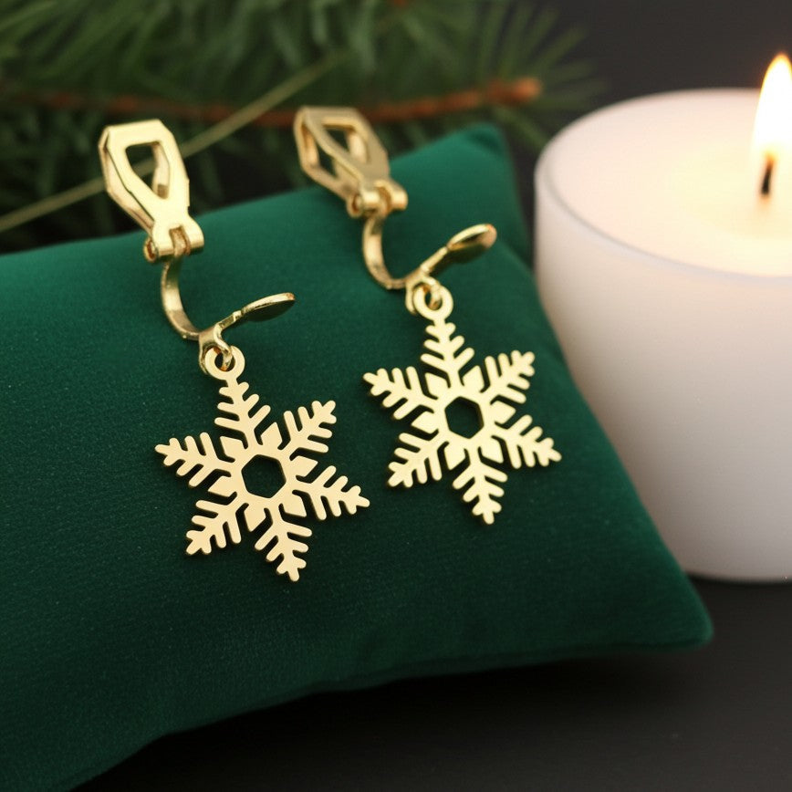 Clip on gold snowflake earrings on a green cushion with a candle in the background