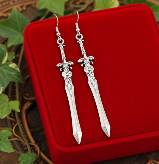 Medieval style fantasy silver sword earrings on a red velvet surface with green leaves in the background